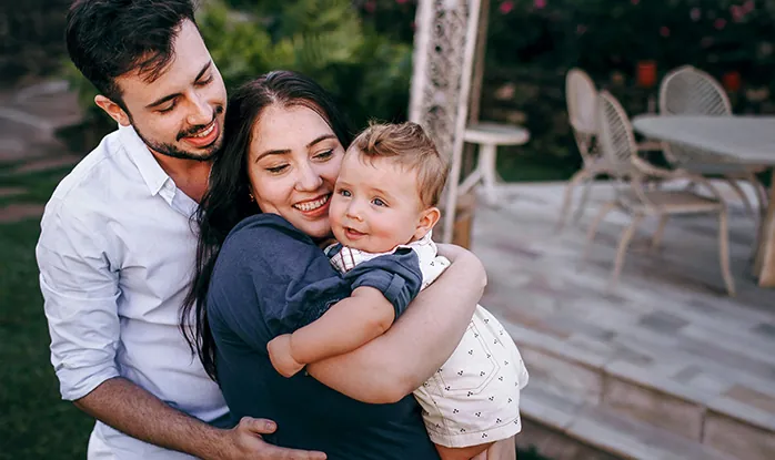 Familia abrazada y sonriendo, con un bebé en brazos